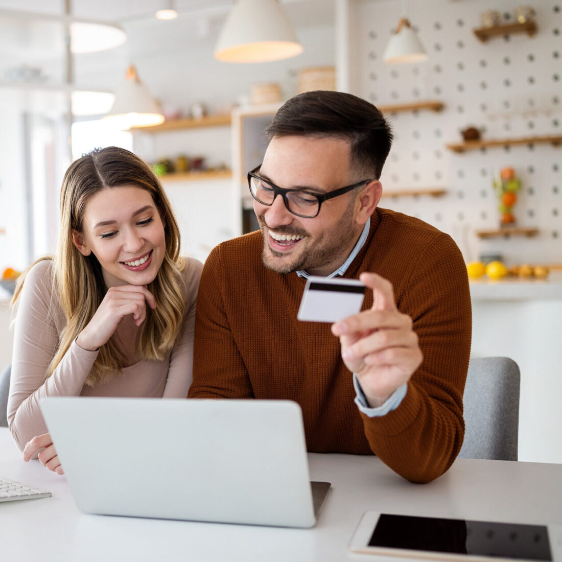 Portrait von einem Pärchen, dass freudig vor dem Laptop im Büro online shopping betreibt