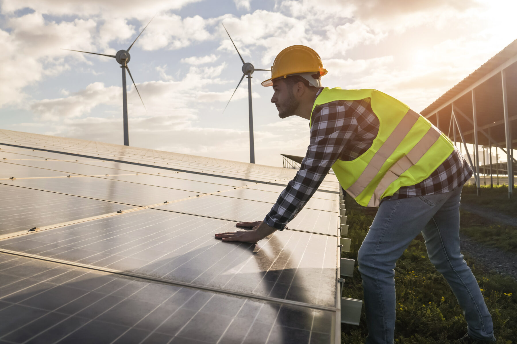 Ein Mann in Sicherheitskleidung, der gerade an Solarparneelen und Windenergieanlagen arbeitet