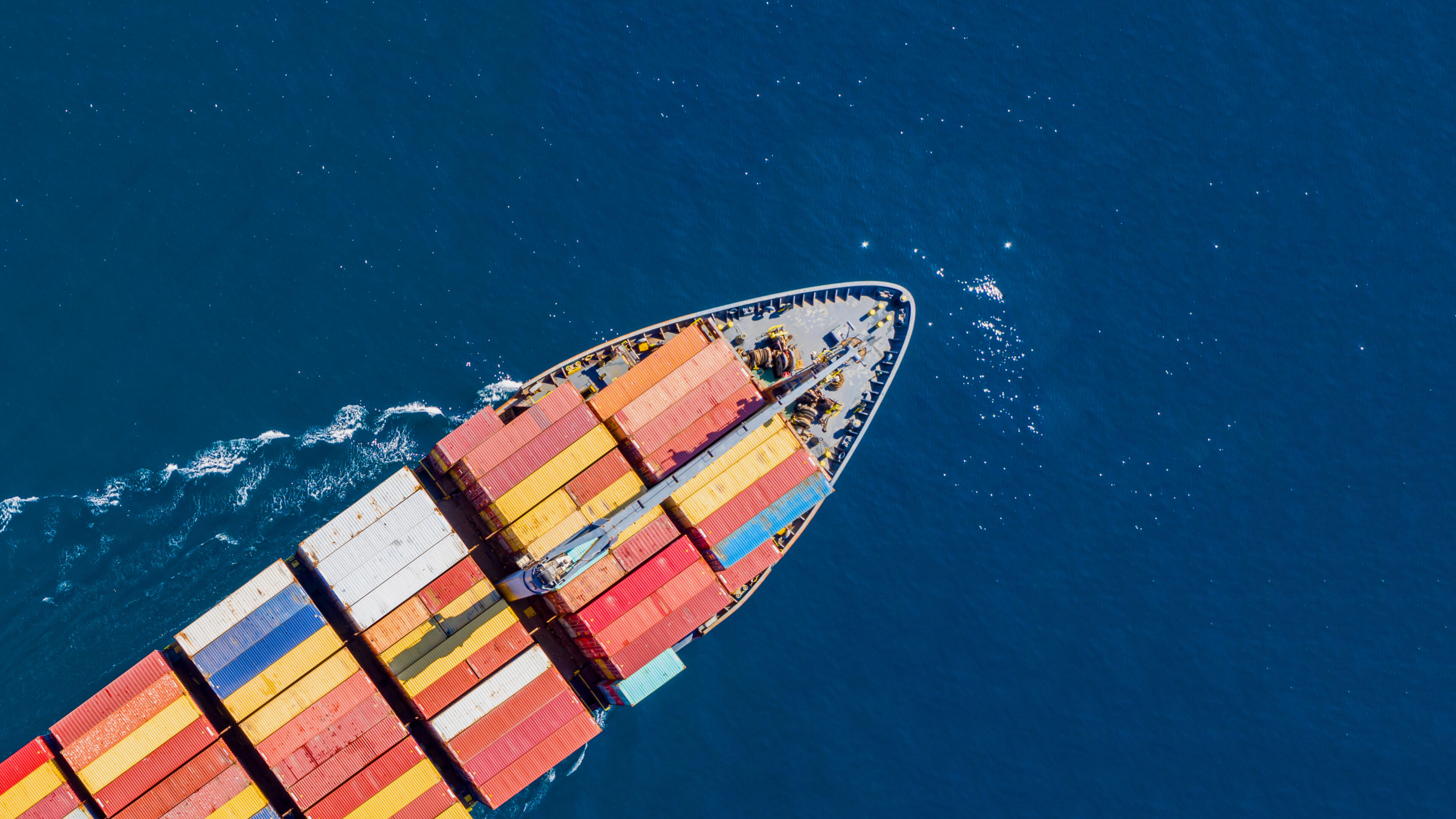 Vogelperspektive eines Frachtschiffes voll beladen mit Containern auf hoher See