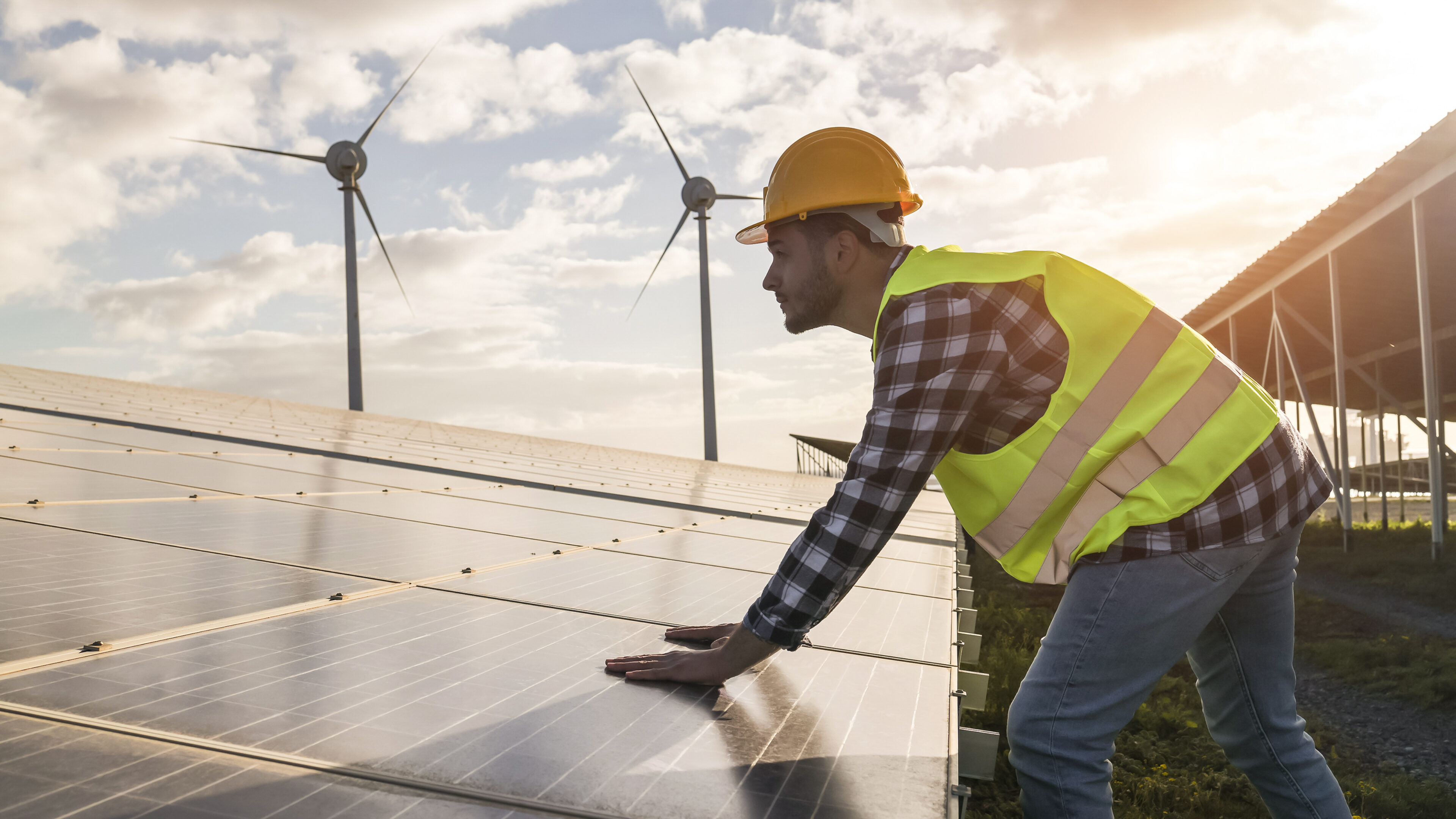 Ein Mann in Sicherheitskleidung, der gerade an Solarparneelen und Windenergieanlagen arbeitet