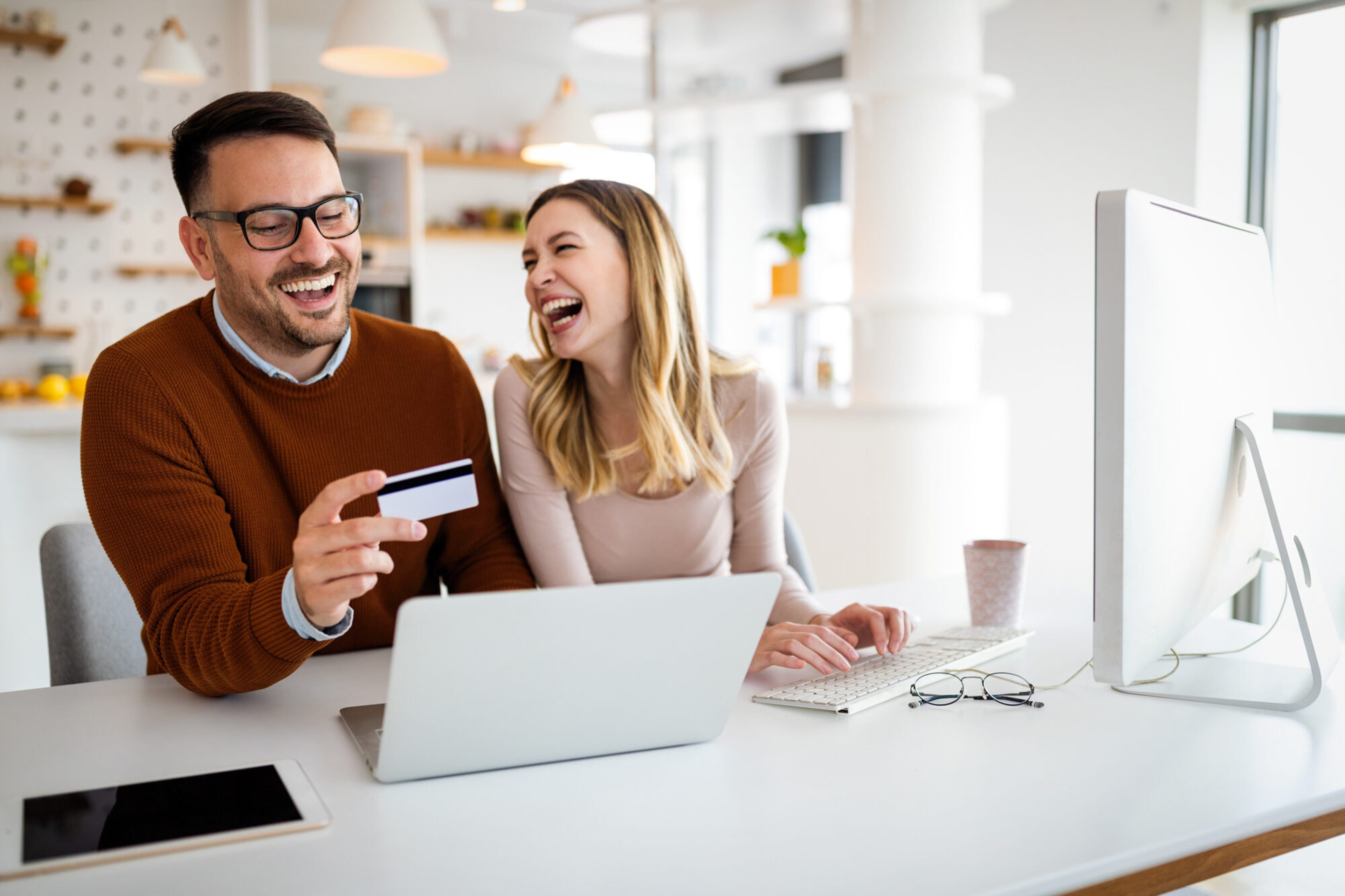 Portrait von einem Pärchen, dass freudig vor dem Laptop im Büro online shopping betreibt