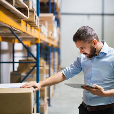 Mann in einem Handelslager mit Tablet, der ein Paket begutachtet