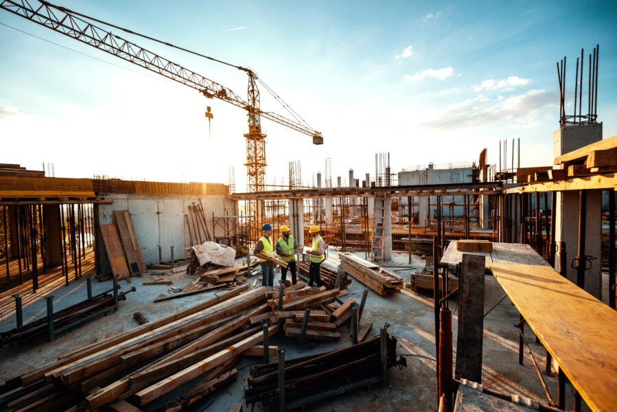 Aufnahme von einer großen Baustelle Menschen in Sicherheitskleidung, mit Baumaterial und einem Kran im Hintergrund