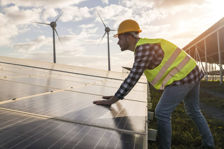 Ein Mann in Sicherheitskleidung, der gerade an Solarparneelen und Windenergieanlagen arbeitet