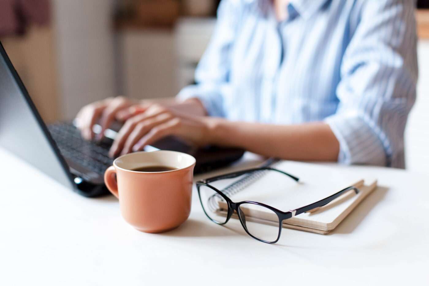 Frau vom Remote-Arbeitsplatz in der Küche mit Laptop, Tasse Kaffee, Brille