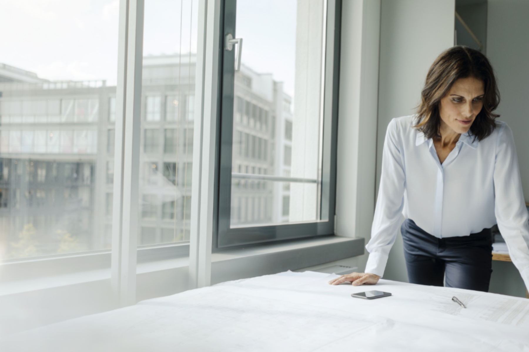 Eine Frau steht in einem Büro an einem Tisch und blickt auf Papiere.