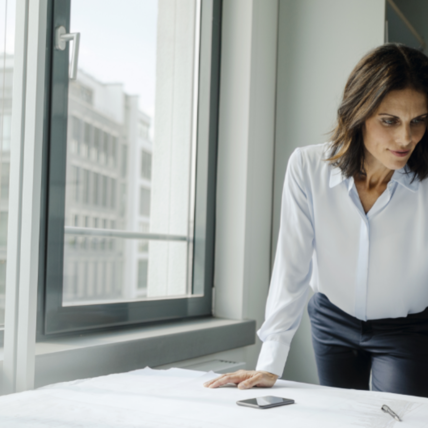 Eine Frau steht in einem Büro an einem Tisch und blickt auf Papiere.