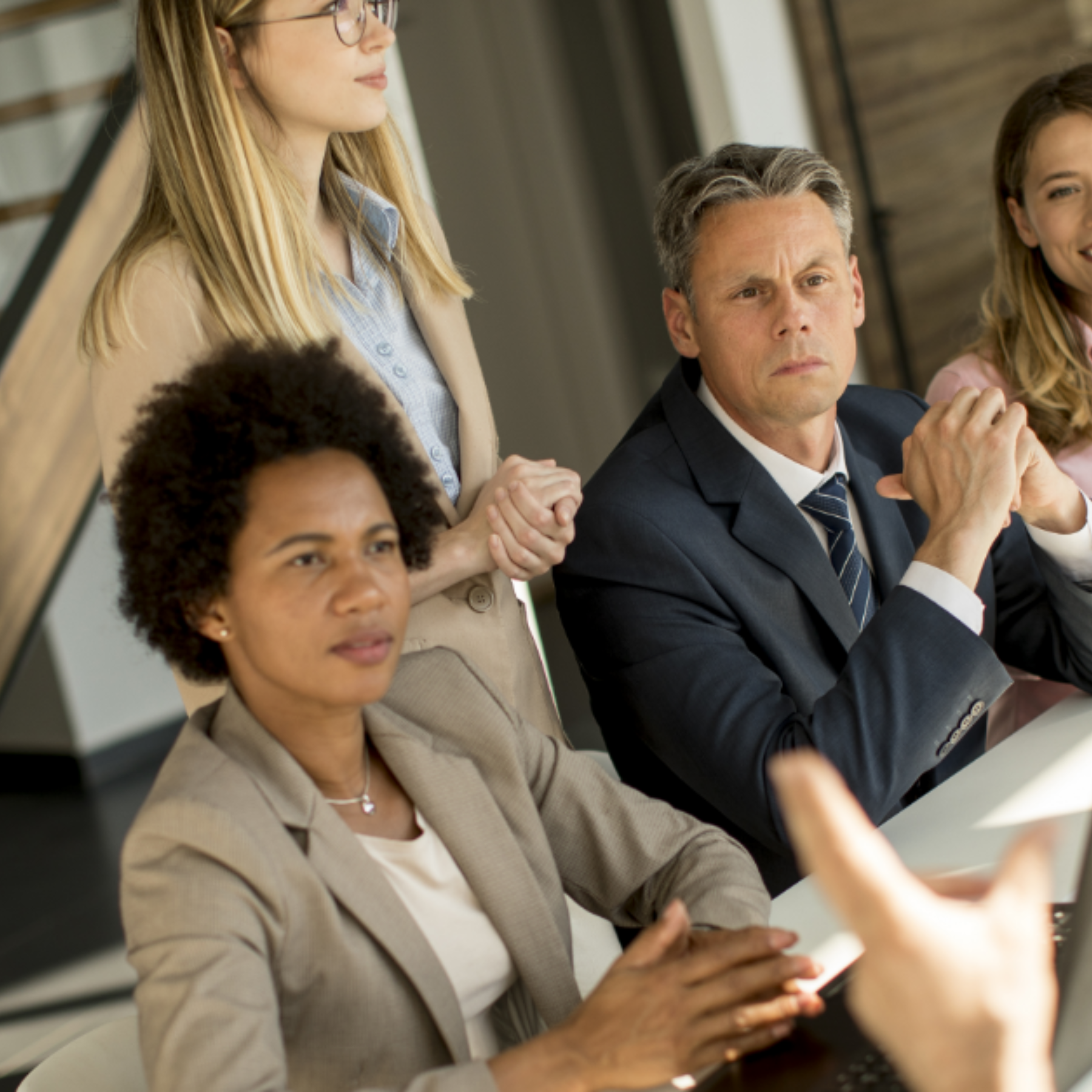 Eine Gruppe von vier Personen sitzt in einem Konferenzraum am Tisch, eine Frau steht hinter ihnen.