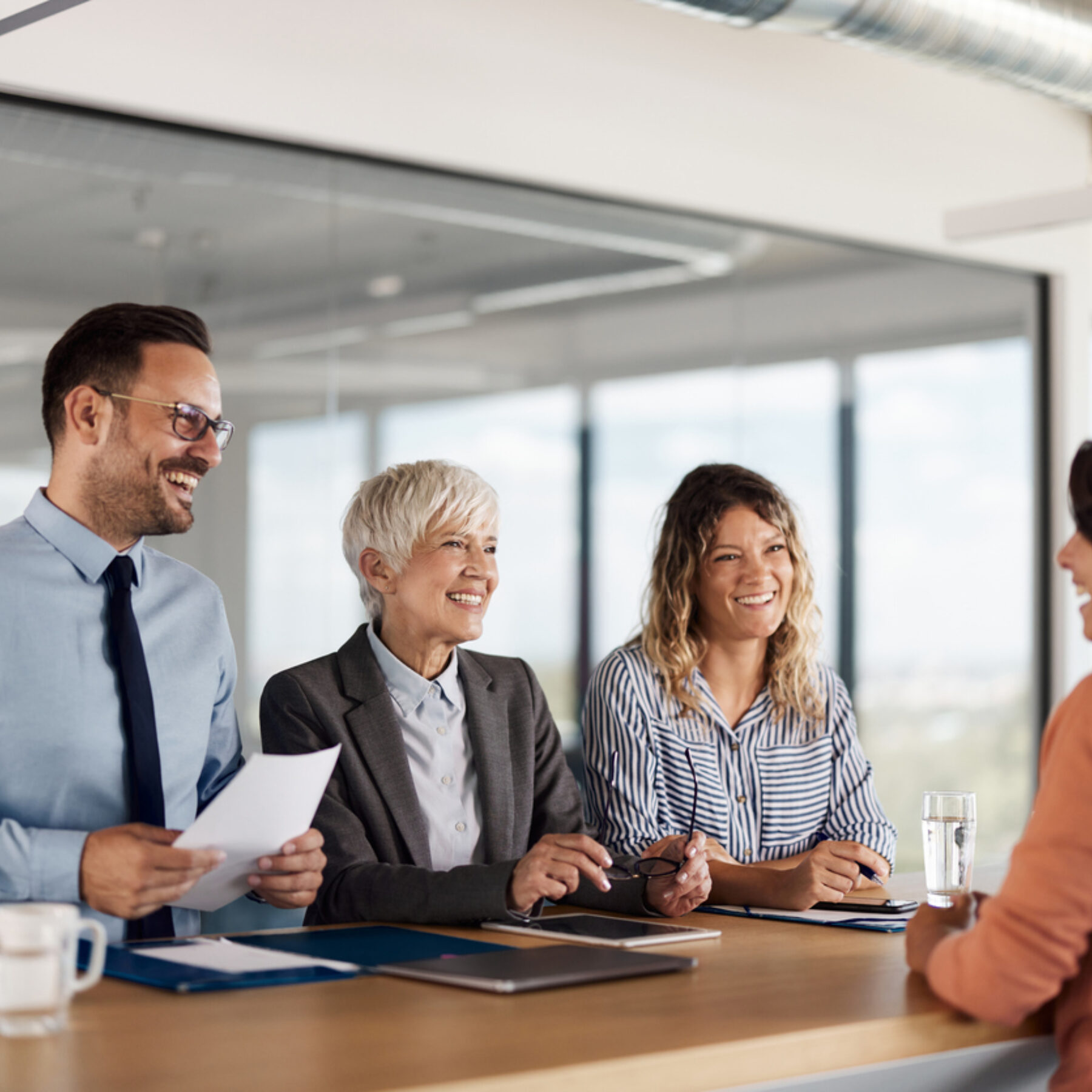 Vier Personen sitzen in einem modernen Konferenzraum an einem Tisch und führen ein Bewerbungsgespräch mit einer weiteren Person, die ihnen gegenübersitzt.