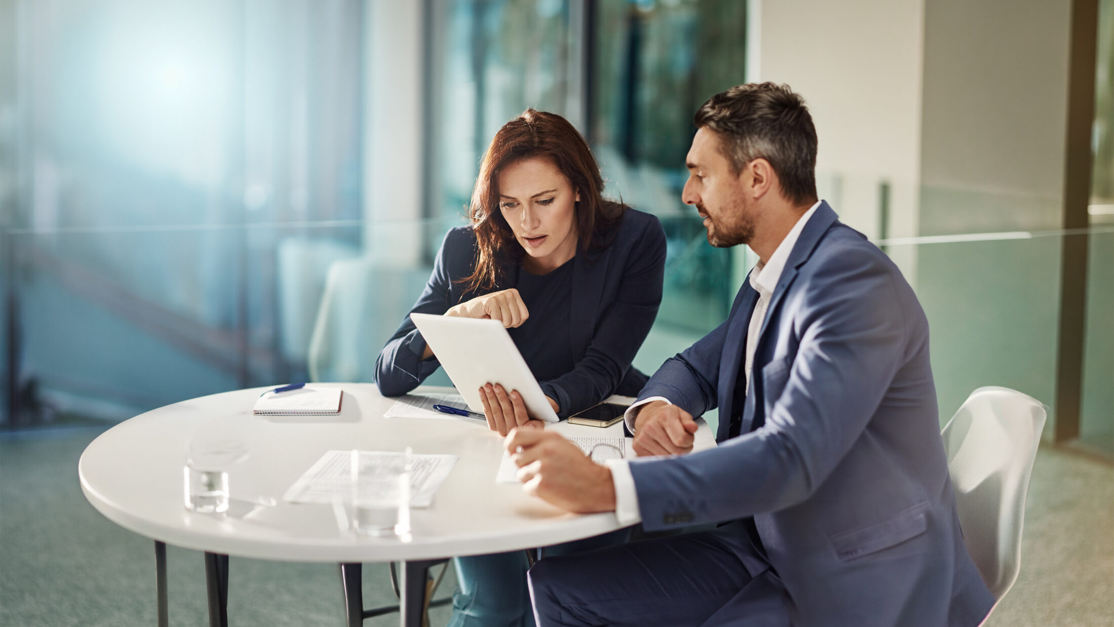 Eine Frau und ein Mann sitzen in einem Büro an einem Tisch und sprechen miteinander.