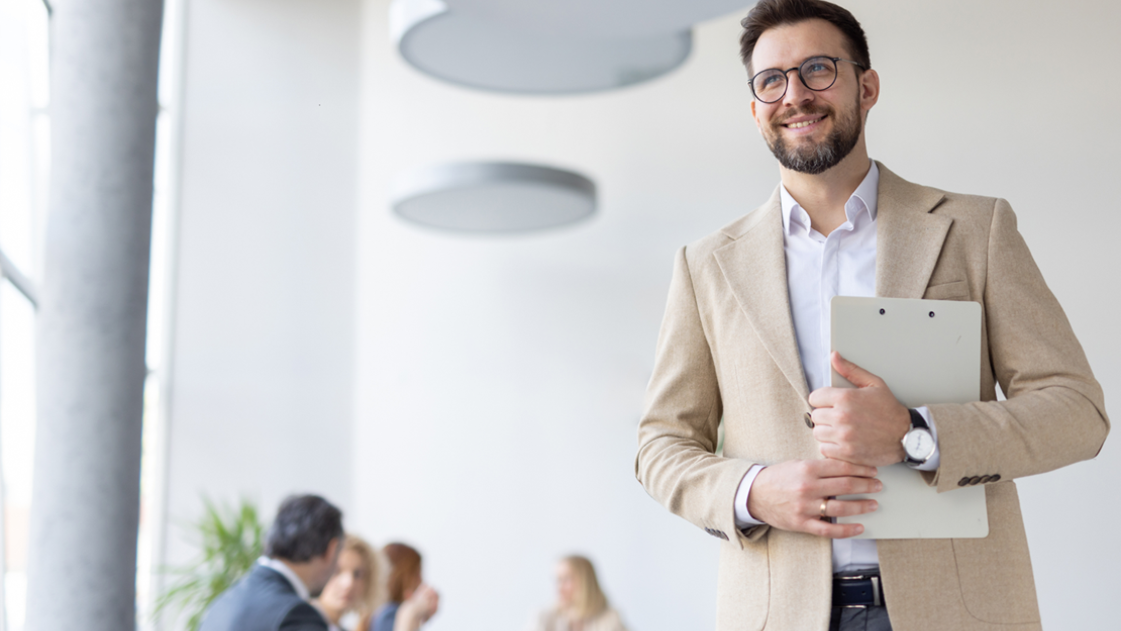 Ein Mann mit Brille und Sakko trägt einen Laptop und lächelt.