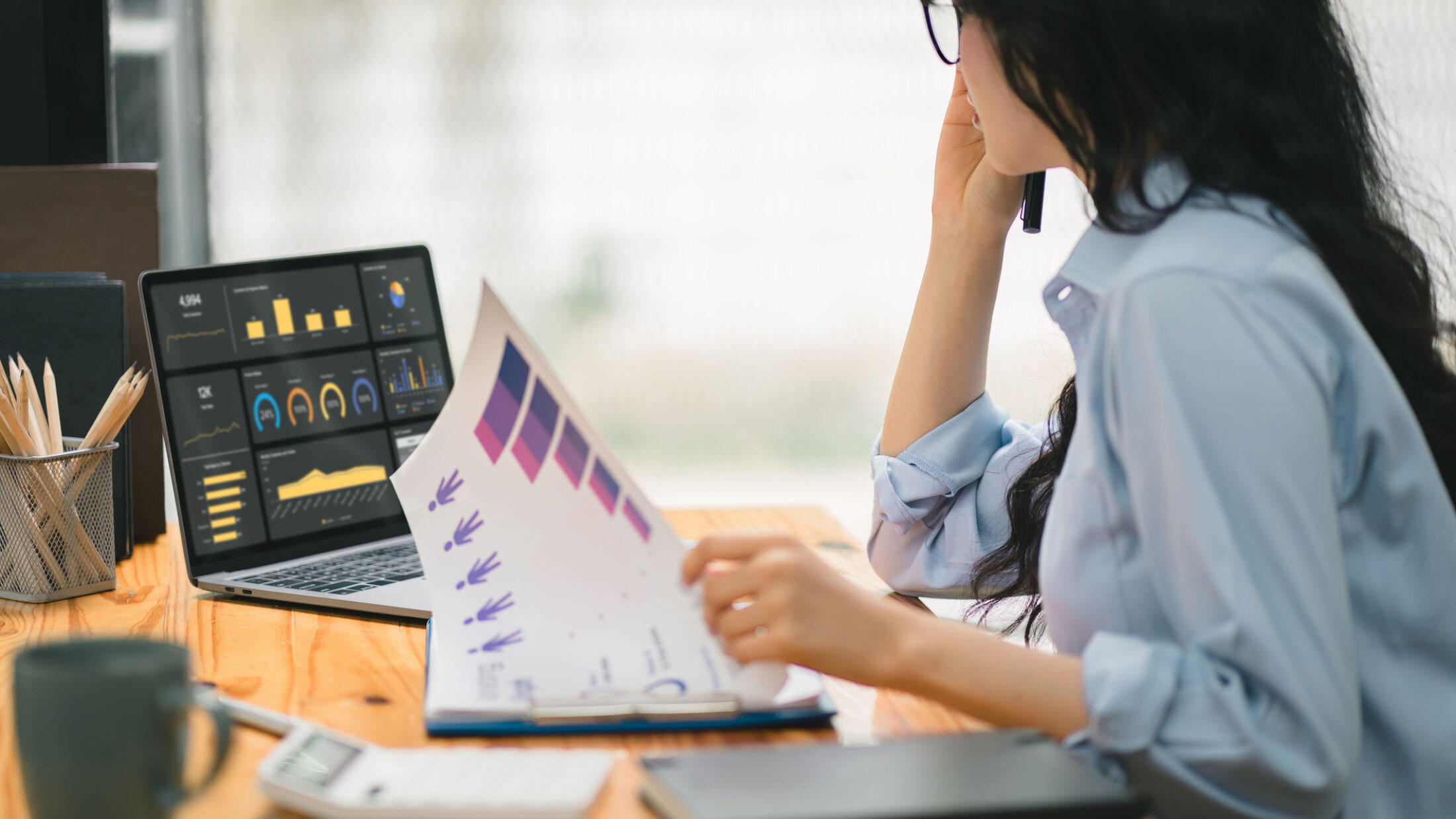 Businesswoman accountant using a calculator, graphs, and charts to analyze market data, balance sheets,accounts,and net profits in order to plan new sales strategies