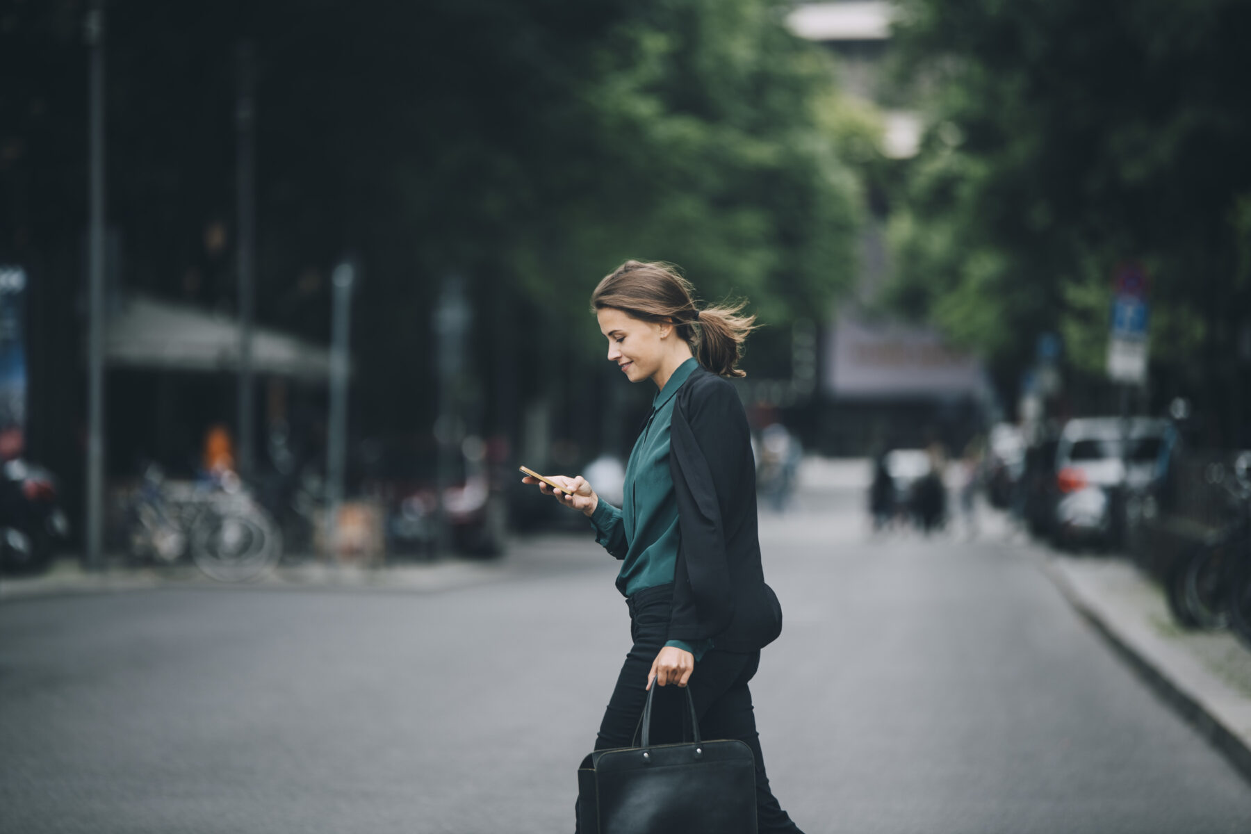 Frau in Business-Look schlendert freudig über die Straße, während sie auf ihr Smartphone schaut