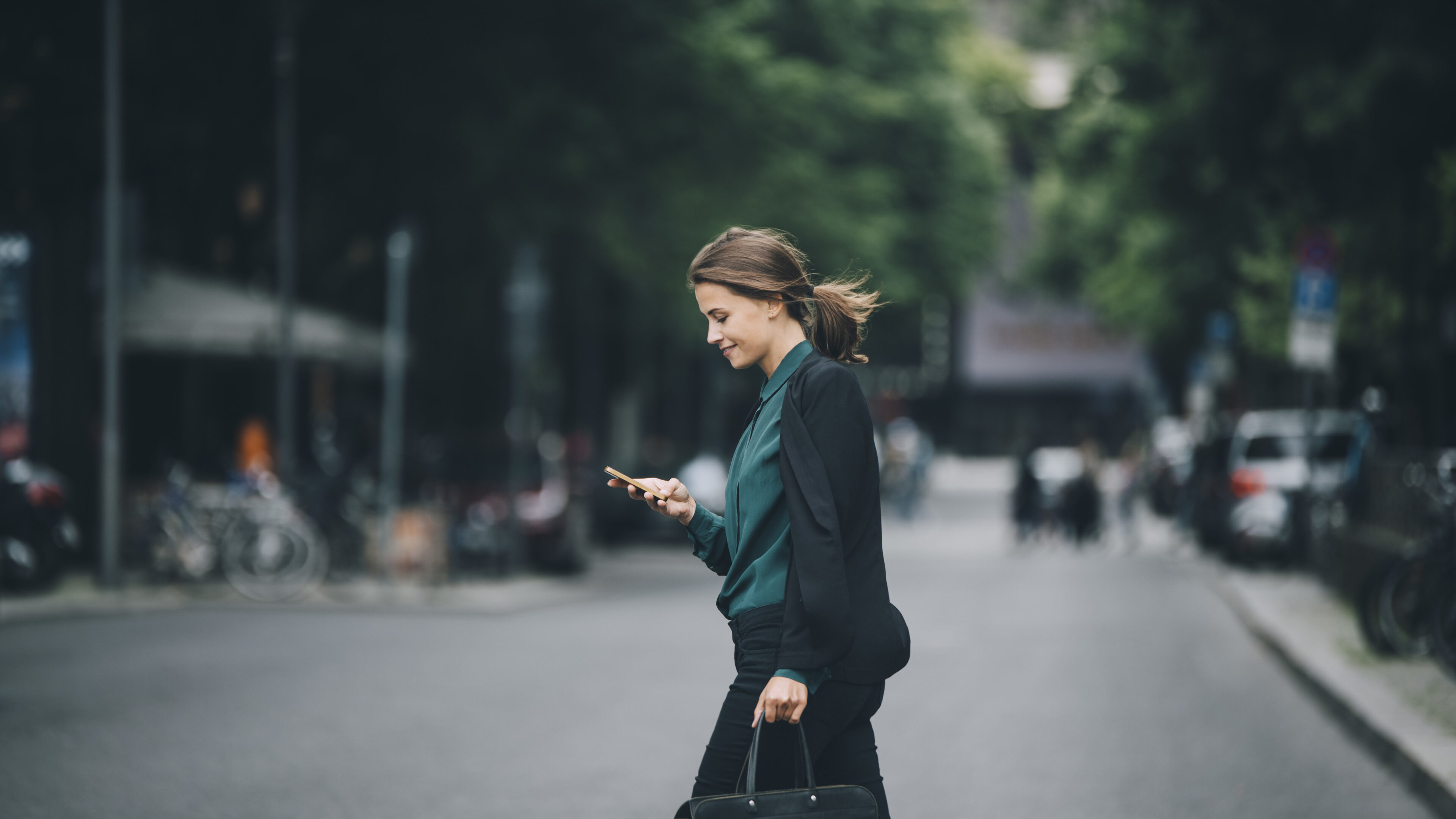 Frau in Business-Look schlendert freudig über die Straße, während sie auf ihr Smartphone schaut